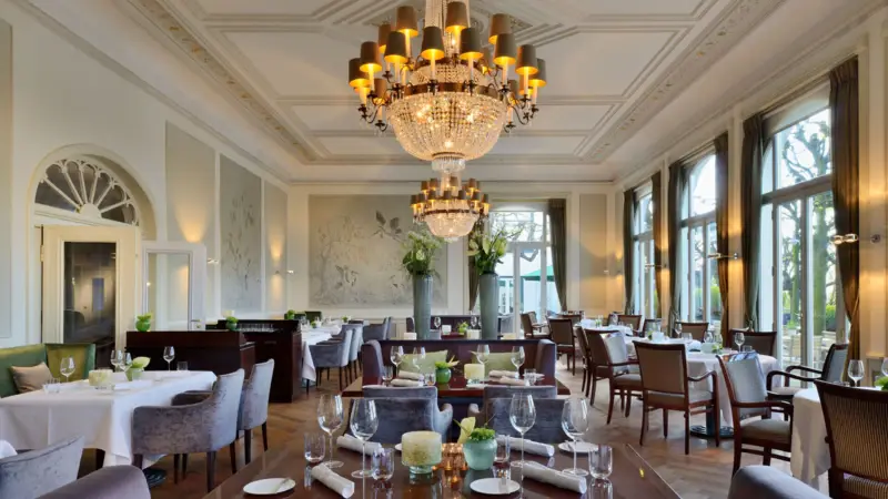 A well-appointed room featuring elegantly set tables and chairs beneath ornate chandeliers.