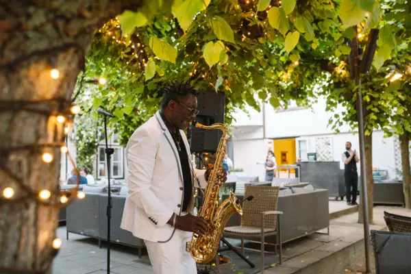 A man playing a saxophone under a tree.
