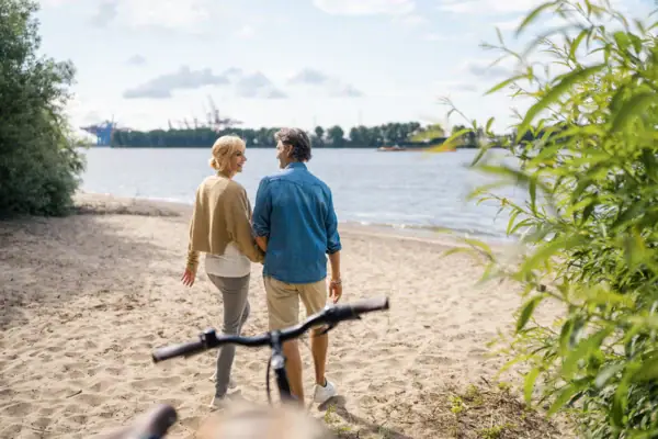 A woman and a man are standing on a beach, looking out at the water.