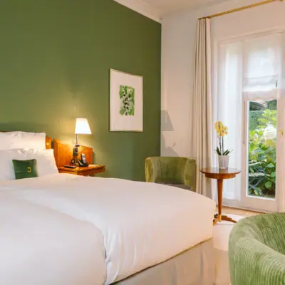 Zimmer Louis C. Jacob Zimmer mit Hotel Louis C. Jacob mit einem Bett vor einer grünen Wand, sowie zwei grünen Sesseln und einem Beistelltisch.