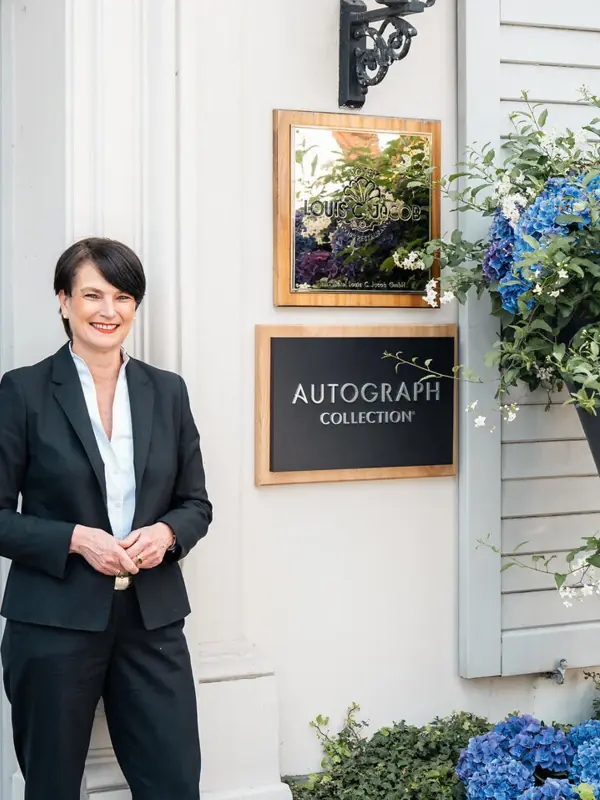 Die Hoteldirektorin Judith Fuchs-Eckhoff steht vor dem Hoteleingang des Louis C. Jacobs und lächelt..