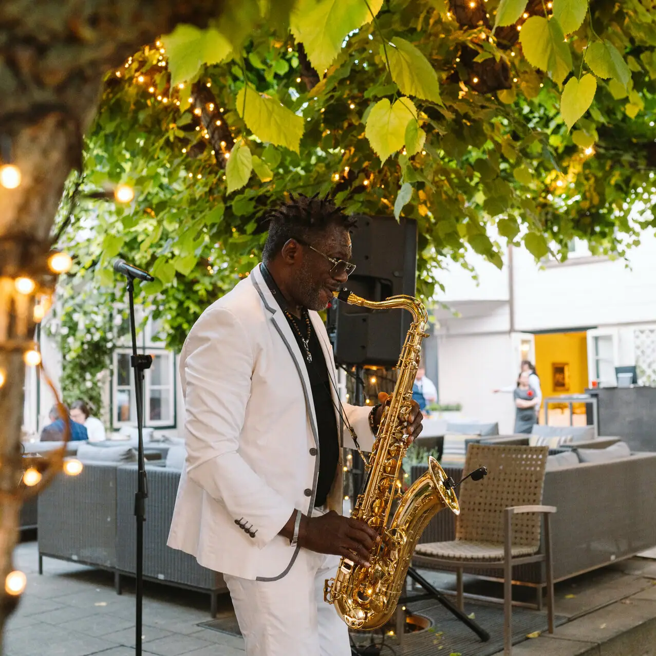 Ein Mann spielt Saxophon unter einem Baum auf der Lindenterrasse.