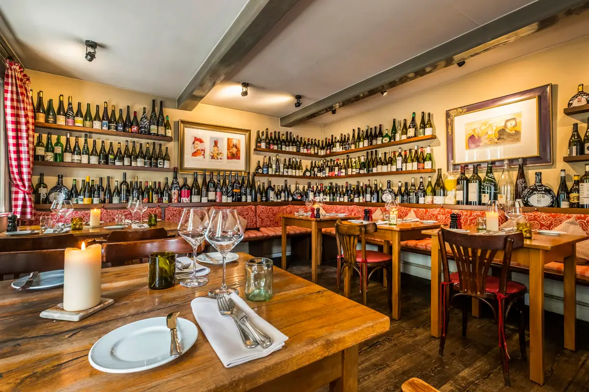 A restaurant interior with neatly arranged tables and chairs, featuring bottles and tableware.