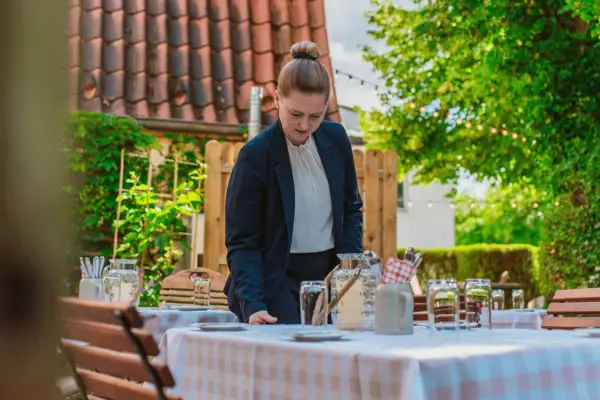 A woman standing at a table with tableware and a wine glass.