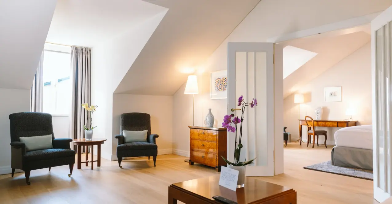 Hotel room in the Louis C. Jacob with a wooden floor, a table, chairs and a vase of flowers.