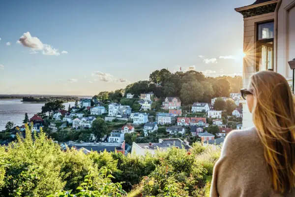 Eine Frau blickt bei Sonnenschein auf das Treppenviertel in Hamburg Blankenese und die Elbe.