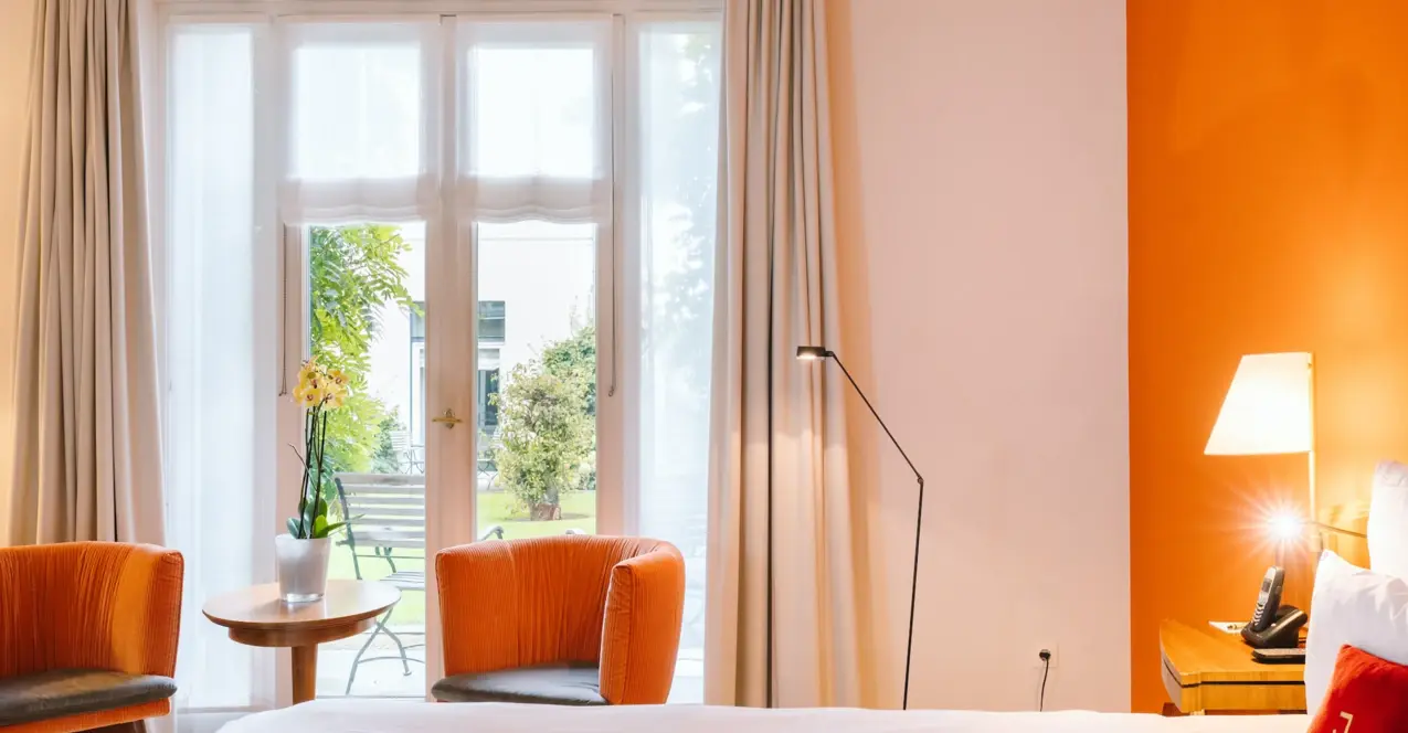 Interior view of a hotel room at the Louis C. Jacob with a bed, table, chairs and a terrace overlooking the garden.