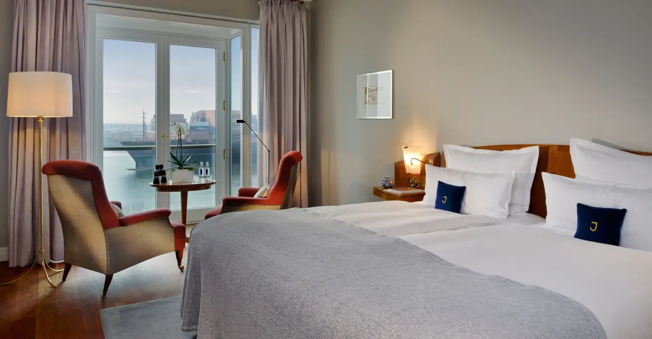 Elegant hotel room in the Louis C. Jacob with a bed, chairs and a window overlooking the Elbe.