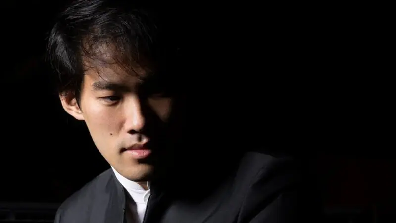 Bruce Liu Pianist Bruce Liu sitzt halb im Schatten und schaut nach unten.