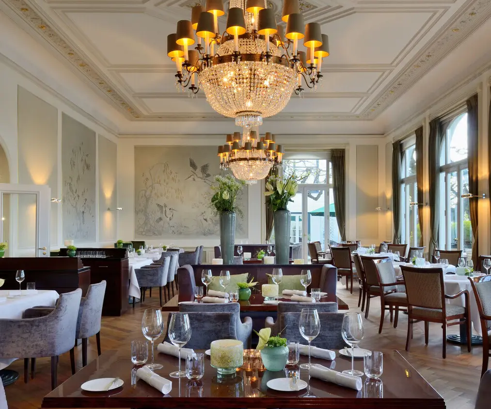 A room with elegantly arranged tables and chairs under ornate chandeliers.