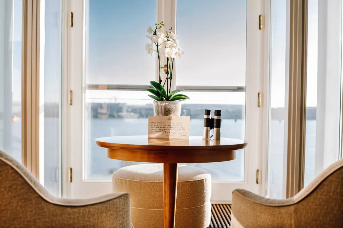 Ein Tisch mit einer Orchidee und einem Fernglas darauf mit der Elbe im Hintergrund