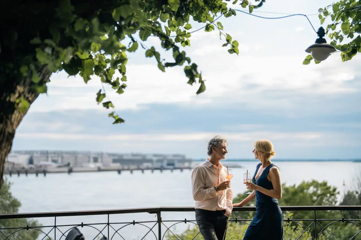 A man and a woman are standing on a railing by a body of water.