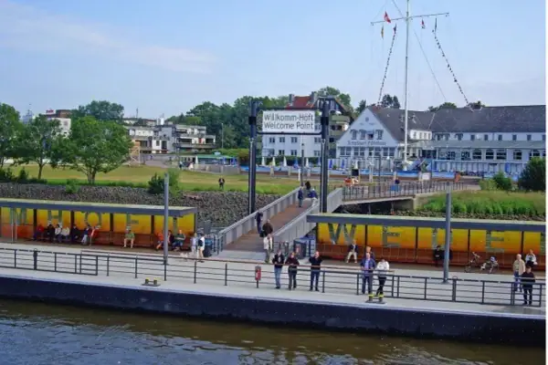 Menschen stehen an der Reling des Pontons vor der Schiffsbegrüßungsanlage Willkommhöft in Wedel und schauen auf die Elbe.