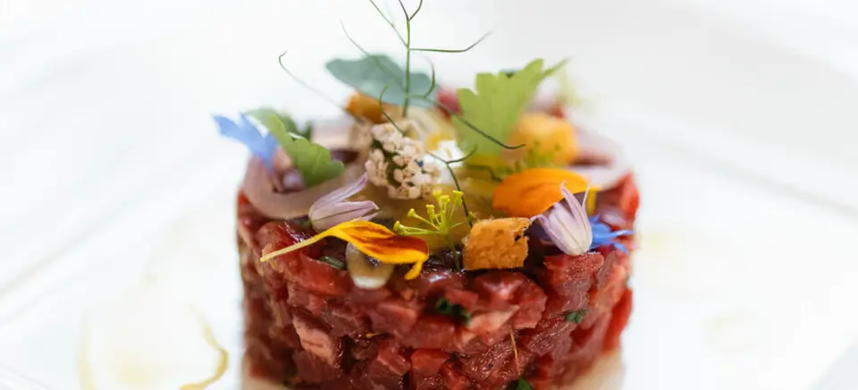 Steak tartare with garnish on a white plate.