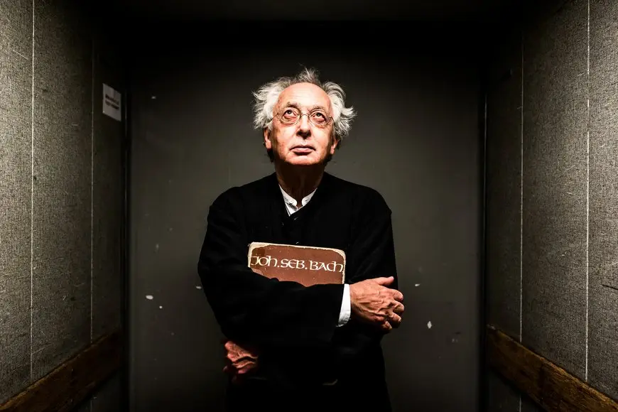 Philippe Herreweghe Ein Mann mit verschränkten Armen hält ein Buch und schaut nach oben.