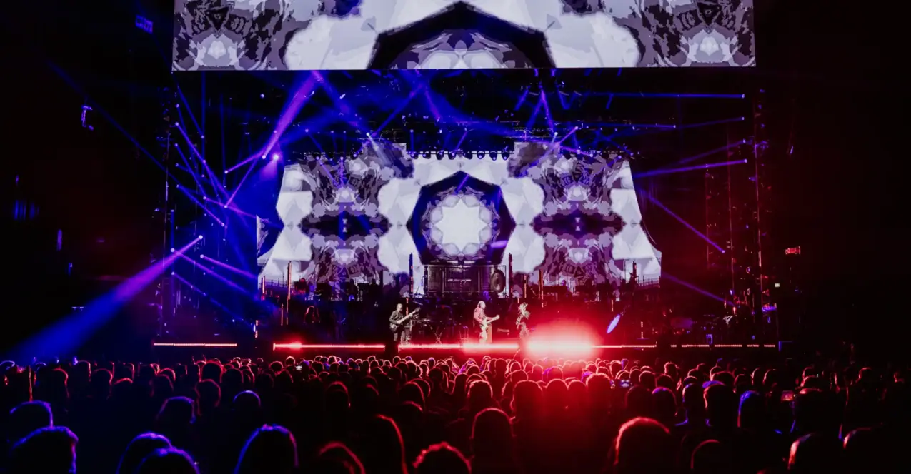 A large crowd stands in front of a red and purple illuminated stage with a band.