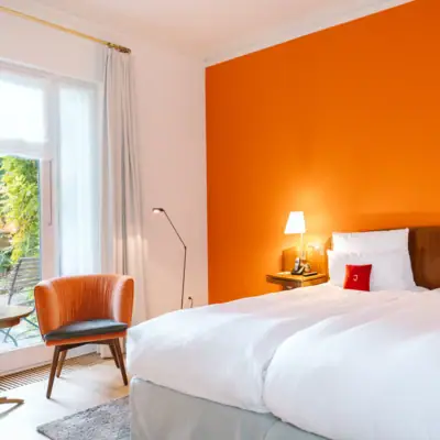 Doppelzimmer Garten Ein helles Hotelzimmer im Hotel Louis C. Jacob mit gemütlichem Doppelbett, einer orangefarbenen Wand und einer kleinen Terrasse.