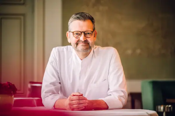 A man in a white shirt smiling indoors.