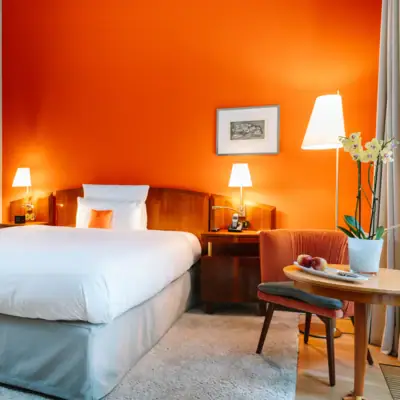 Zimmer Louis C. Jacob Zimmer mit orangener Wand, einem Bett, einem Stuhl und Beistelltisch im Hotel Louis C. Jacob.