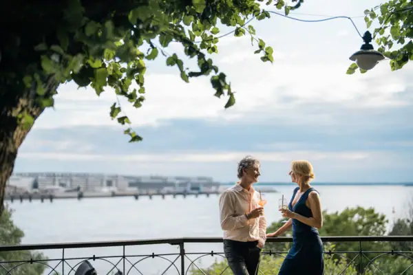 A man and woman standing on a railing by a lake under a cloudy sky.