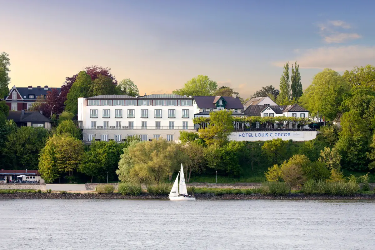 Außenansicht vom Louis C. Jacob Hotel mit einem Segelboot auf der davorliegenden Elbe.