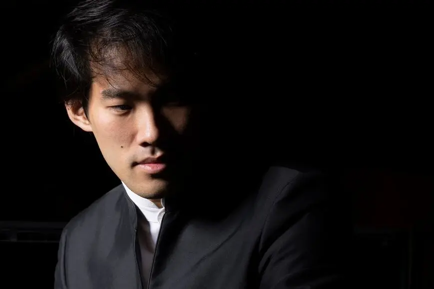 Bruce Liu Ein Mann in Anzug steht vor einem schwarzen Hintergrund.