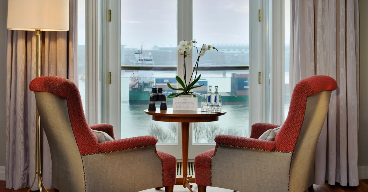 Hotel room at the Louis C. Jacob with two chairs and a table in front of a window with a view of the Elbe.