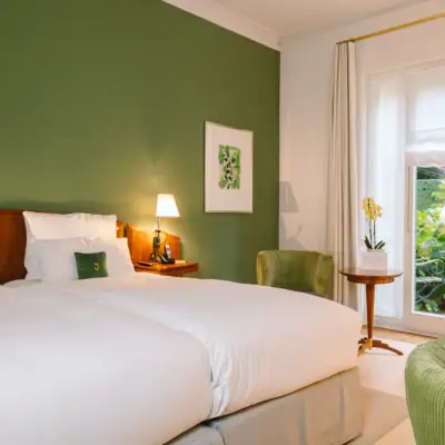 Ein Zimmer mit Bett im Hotel Louis C. Jacob mit grüner Wand, einem Gemälde und dem Blick in den Garten.