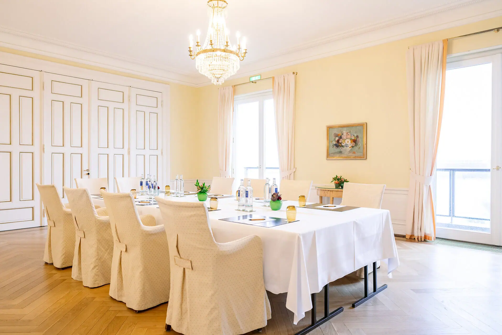 A dining room with a table covered in a tablecloth, surrounded by chairs, and a vase on the table.
