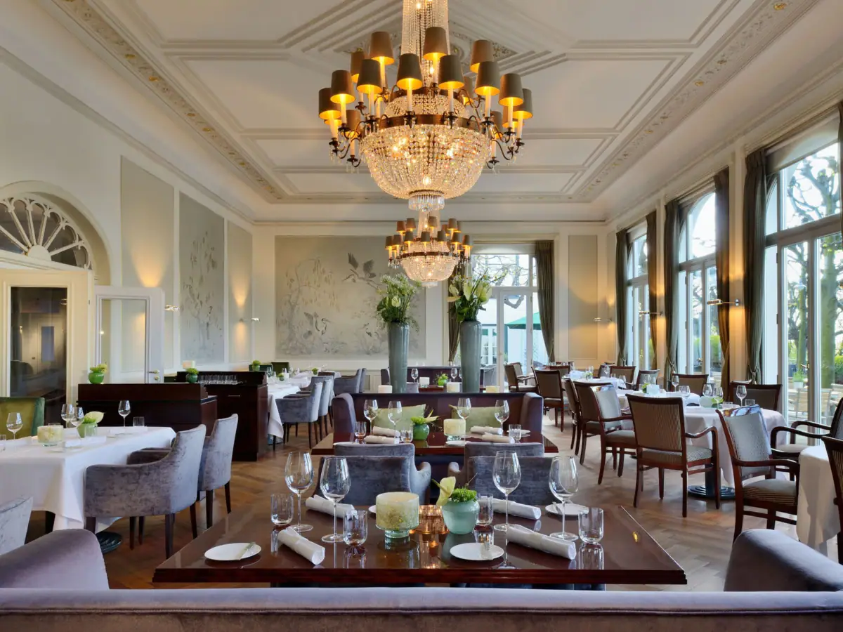 Jacobs Restaurant A room with elegantly set tables and chairs, featuring chandeliers hanging from the ceiling.