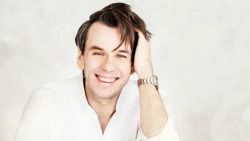 Künstler Benjamin Bernheim lächelt und stütz seinen Kopf auf der linken Hand auf.