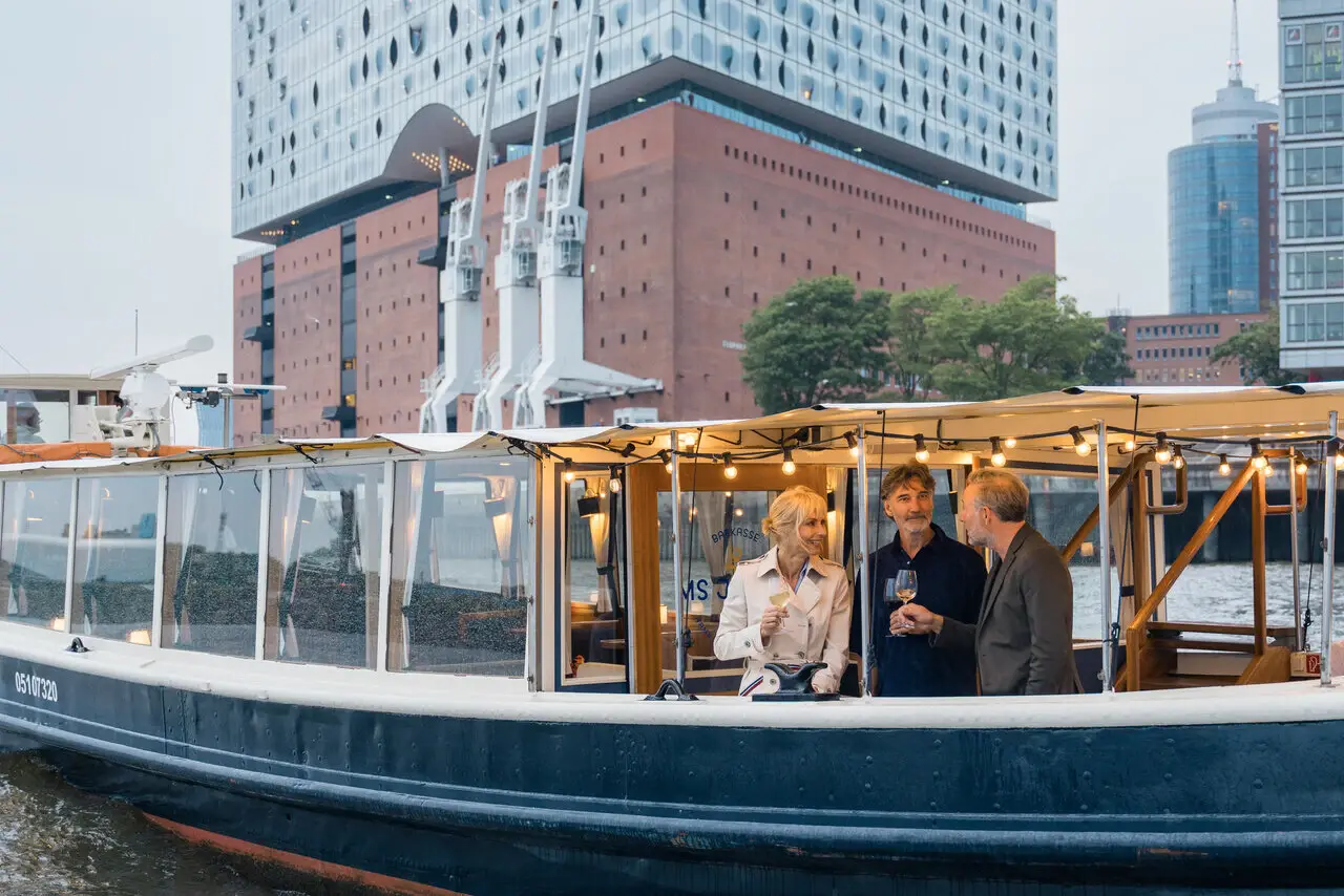 MS Jacob Hamburg A group of people on a boat in front of a building with a clear sky.