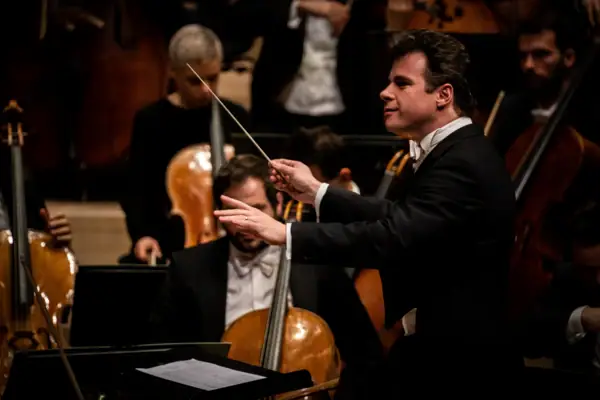 Jakub Hrůša A man is conducting an orchestra of string instruments.