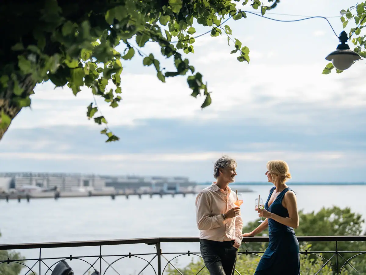 Lindenterrasse A man and woman standing on a railing by a lake.