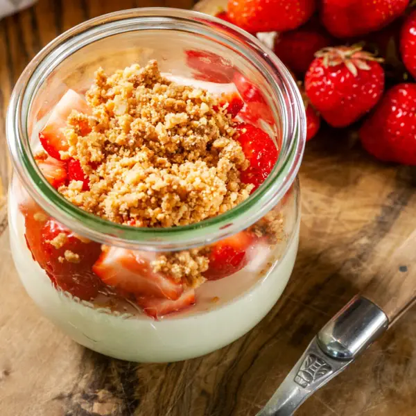 A jar of dessert with strawberries and a spoon.