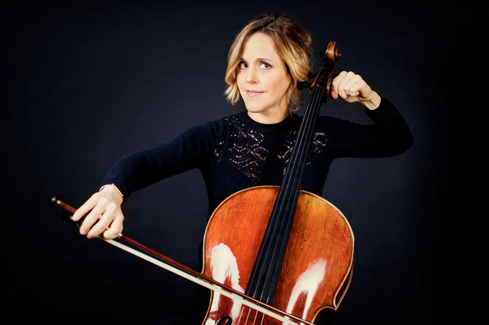 Sol Gabetta Vor einem dunklen Hintergrund sitzt eine Frau, die einen Cello spielt.