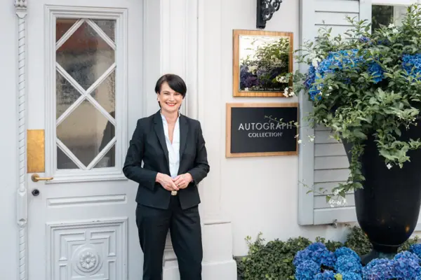 The manager in front of the hotel entrance A woman in a suit is standing in front of a building.