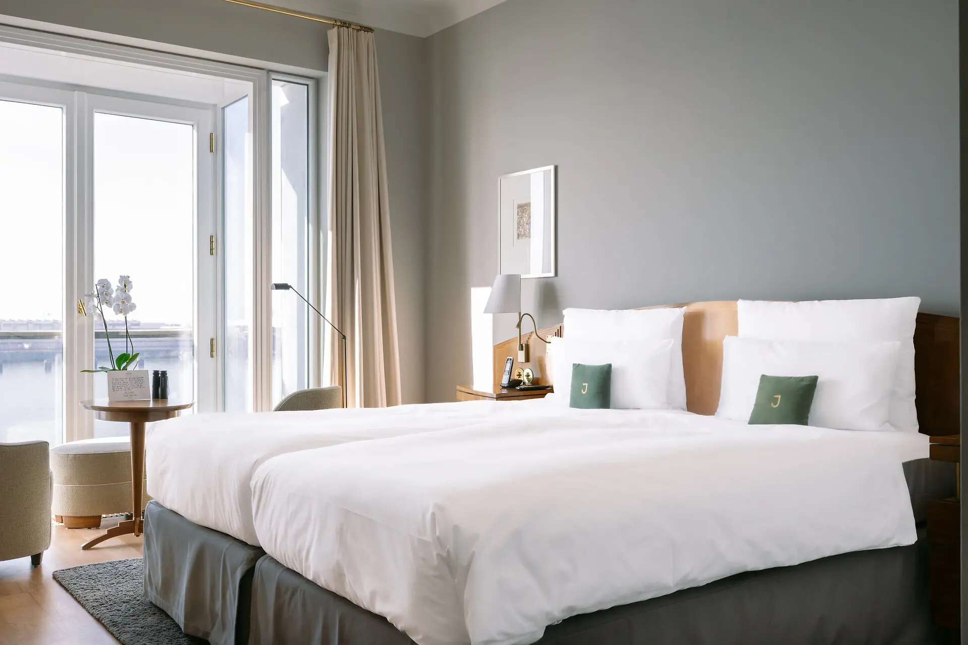 Deluxe double room A bed with white sheets and a lamp on a nightstand.