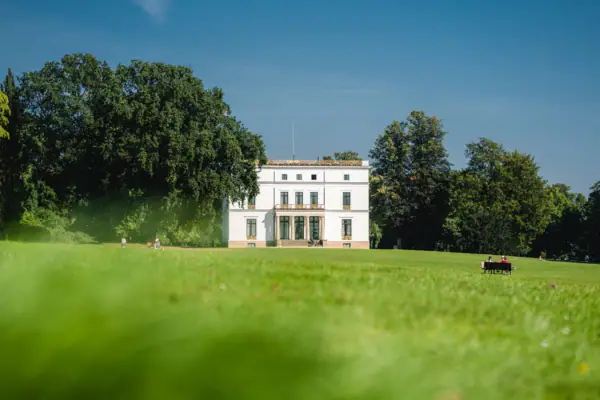 Blick über eine Wiese auf das klassizistische Jenisch-Haus eingerahmt von Bäumen im Jenischpark in Hamburg.