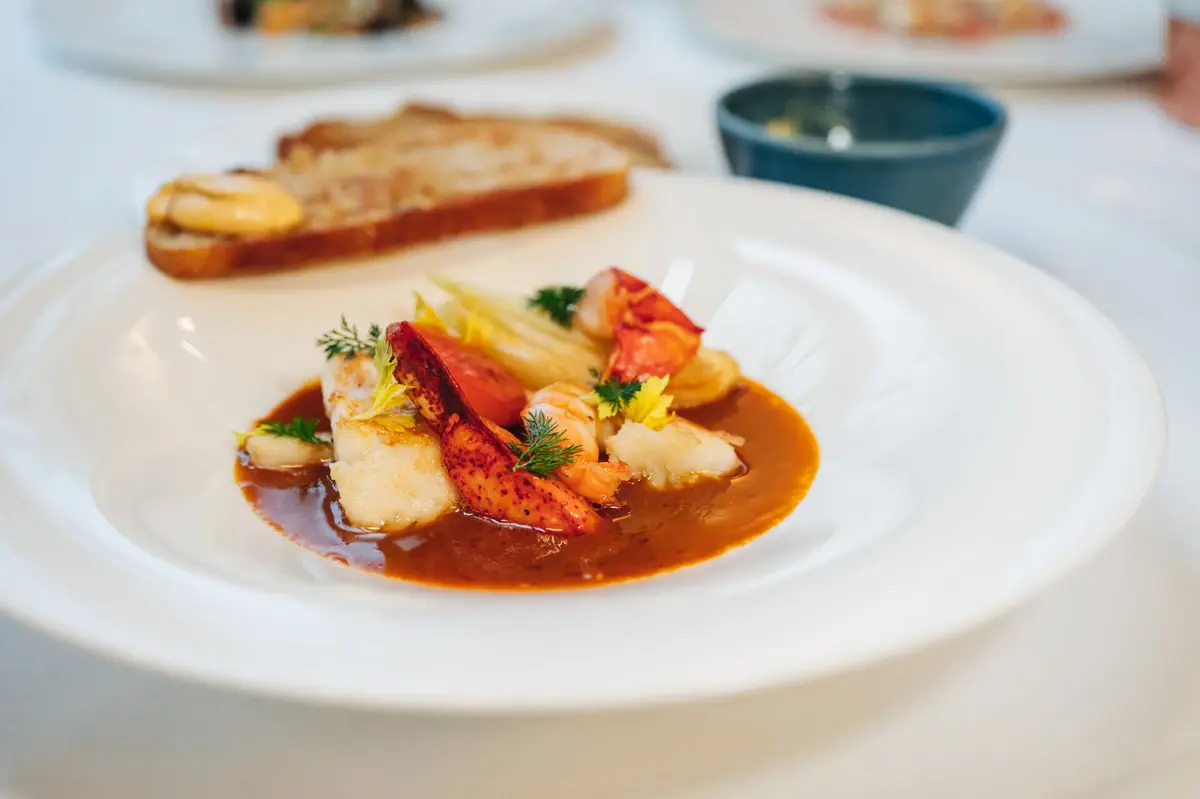 Weißer tiefer Teller mit Fischsuppe und einer Scheibe Brot.