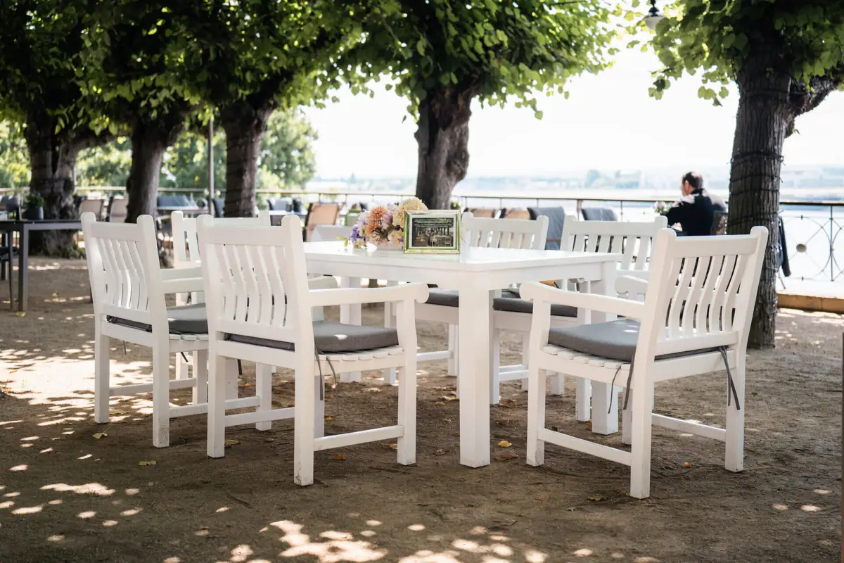White table and chairs under trees in an outdoor setting.