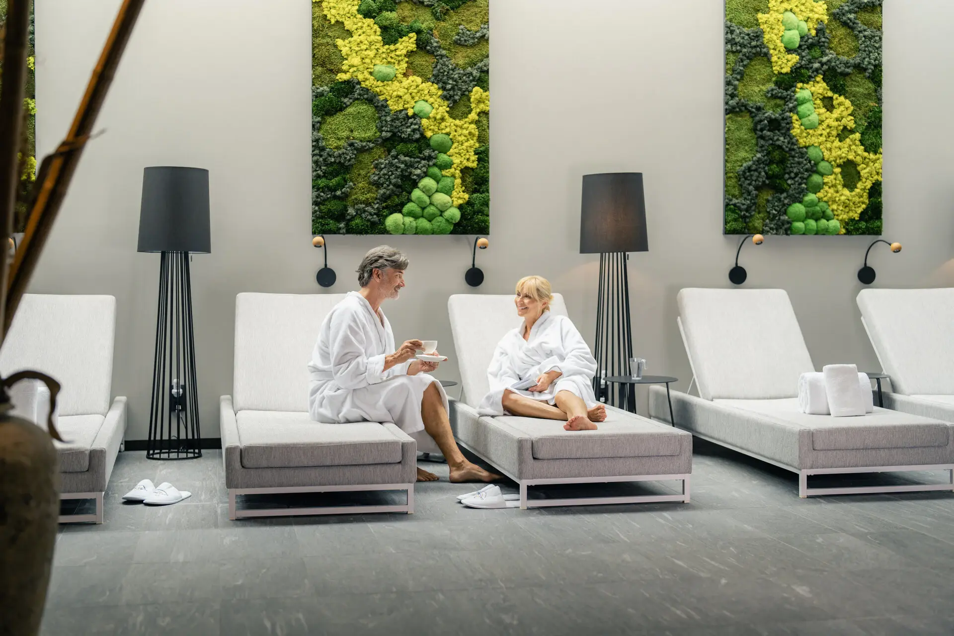 Ein Mann und eine Frau in weißen Bademänteln sitzen auf Entspannungsliegen im Wellness-Bereich des Hotels Louis C. Jacob.