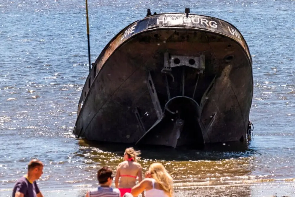 Schiffswrack Uwe am Elbstrand in Hamburg, davor sitzt eine Gruppe von Touristen am Strand..