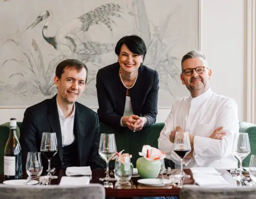 A group of people smiling and posing indoors, some holding wine glasses.