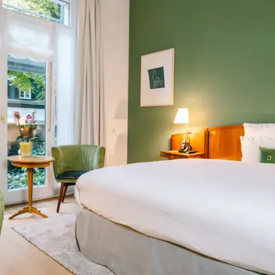 Zimmer im Hotel Louis C. Jacob mit Bett vor einer grünen Wand.