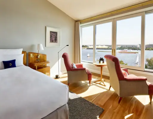 Rooms & Suites A room with a bed and chairs, and a window overlooking the water.