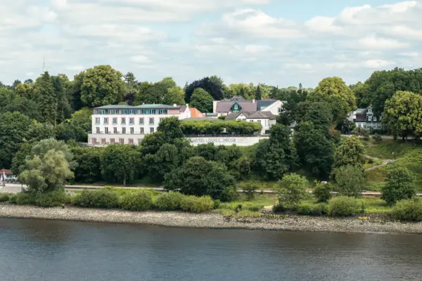 A building near a body of water with trees and a cloudy sky.
