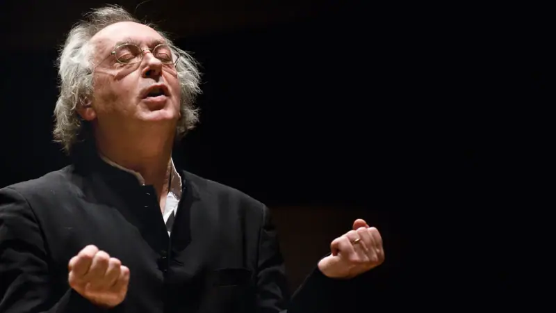Philippe Herreweghe Ein älterer Mann mit Brille und schwarzem Hemd singt mit geschlossenen Augen und hält seine Fäuste vor sich.