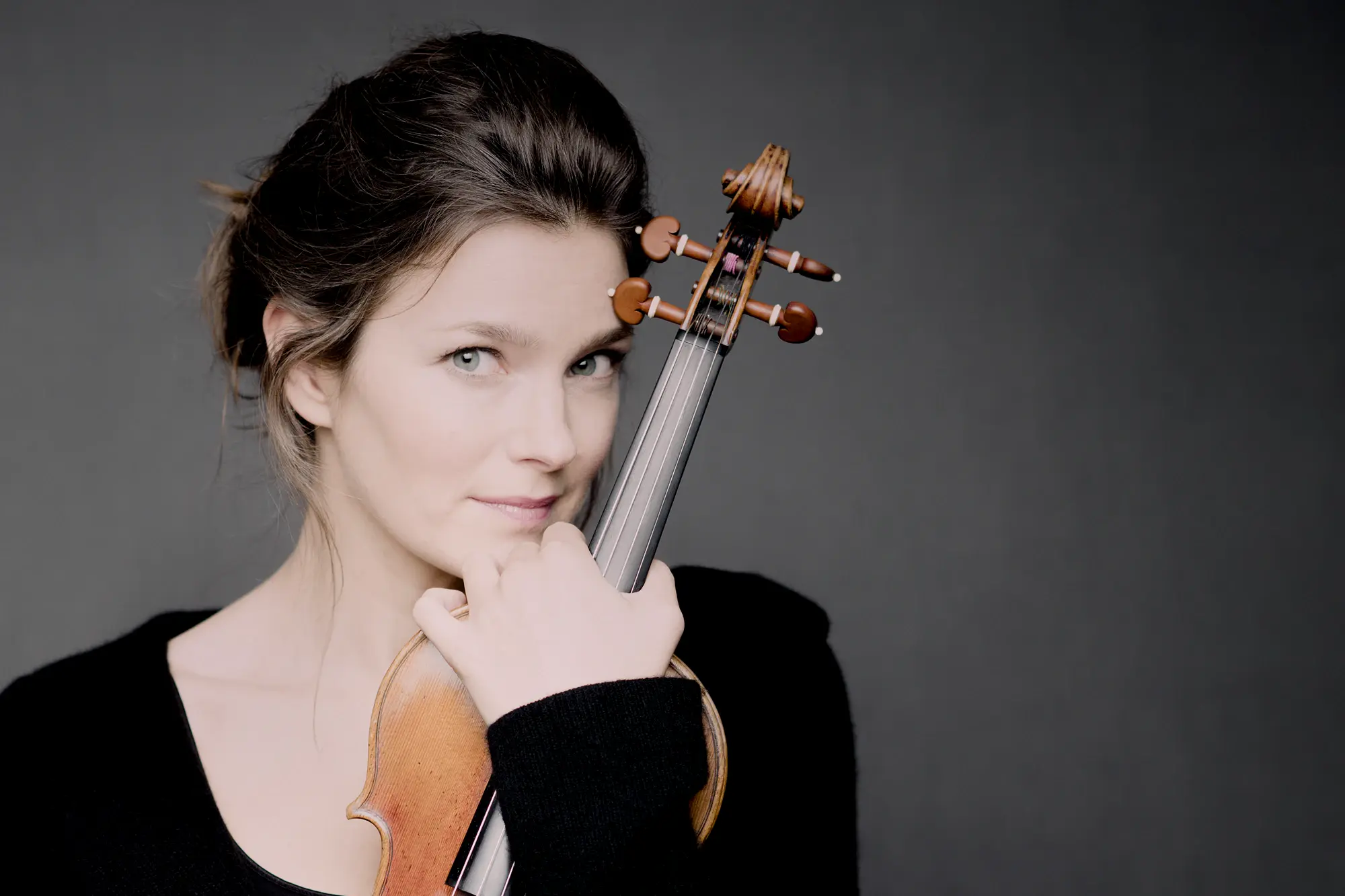 Janine Jansen Janine Jansen steht vor einem grauen Hintergrund und hält eine Geige im Arm.