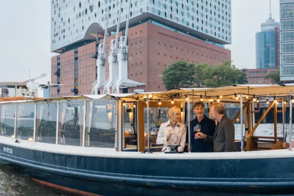 A group of people on a boat in front of a building with a clear sky.